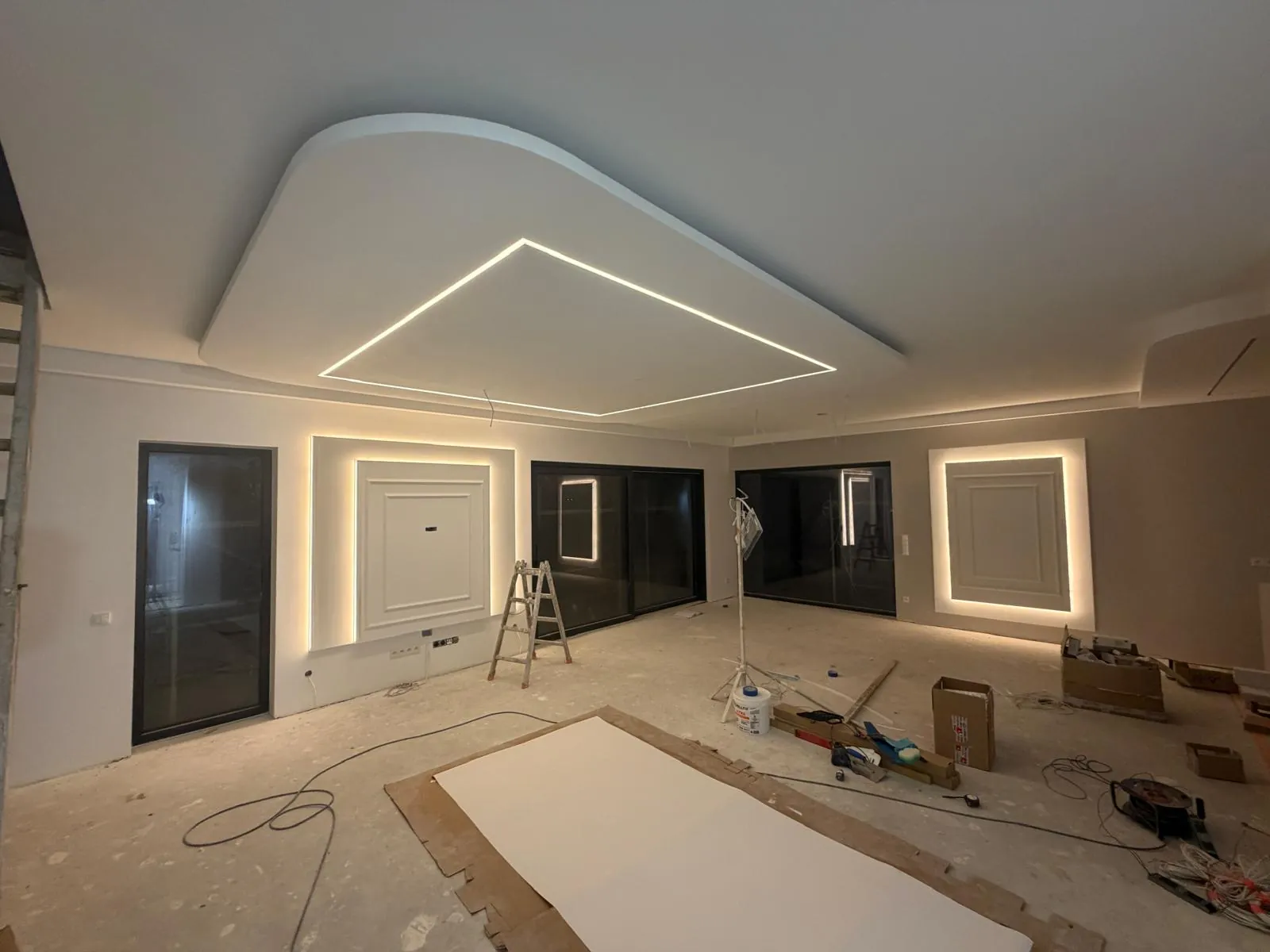 Salon w trakcie wykończenia: sufit podwieszany z liniami LED i podświetlane ramy na ścianach